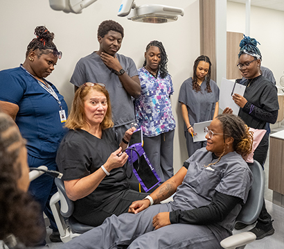 dental assistant students in exam rooms watching instructor give demonstration