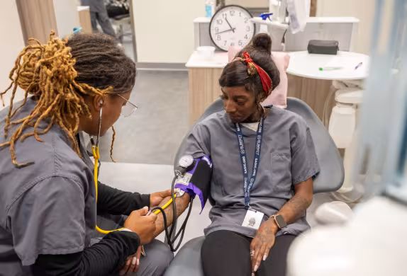 dental assistant student listening to pulse on another student with stethoscope