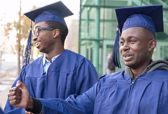 Photo of two smiling Summit Academy students celebrating in caps and gowns outside the venue where commencement was held