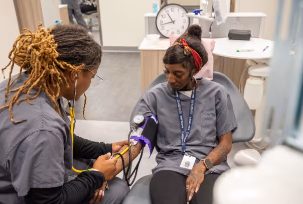 dental assistant student listening to pulse on another student with stethoscope