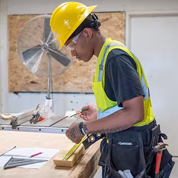 Carpentry student at Summit Academy OIC measuring a piece of wood with a tape measure